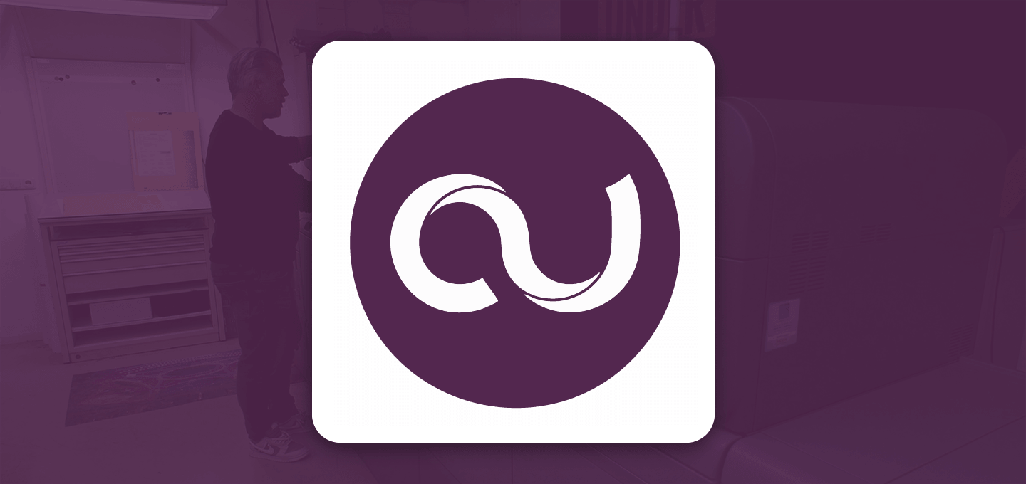 Cards Unlimited logo - Man operating a Ricoh printer in a dimly lit room. The scene is overlaid with a purple tint, and a white logo featuring a stylized "AU" is on the right.