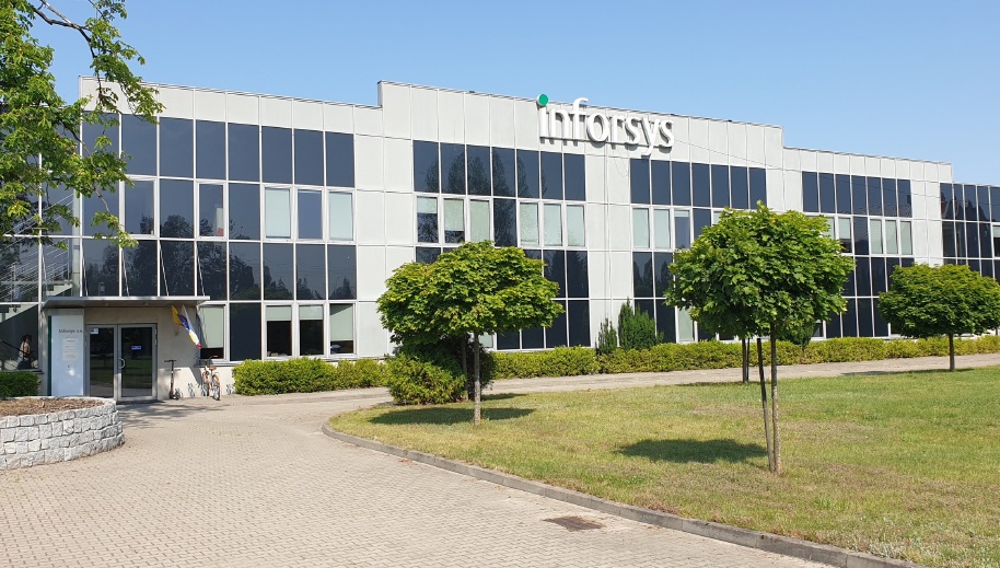Inforsys office building with modern glass facade, green lawn and trees on a sunny day.